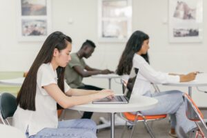 Woman in a White Shirt Sitting on a Chair While Typing on Her Laptop